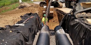 sewer pipe installation, cover pipe with limestone, skid loader, hard hat, excavator