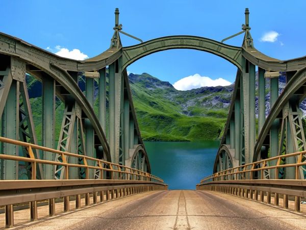 A metal bridge overlooking a serene lake and green mountains under a clear blue sky.