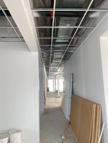 Couloir en construction avec plafond ouvert et matériaux empilés.