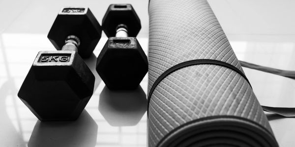 Dumbbells and a rolled yoga mat on a reflective surface.