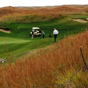 Golfers near a golf cart on a lush green course surrounded by tall grass.
