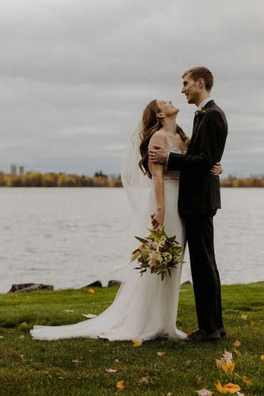 Bride and groom embracing by a lakeside on their wedding day.