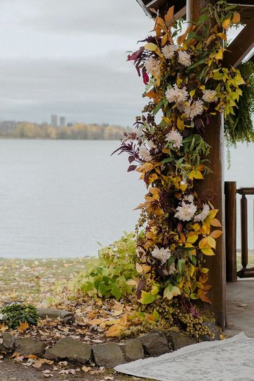 A wooden post decorated with autumn leaves and flowers by a lakeside.