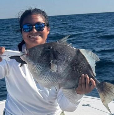 Smiling person proudly holds a large fish on a boat in the ocean.