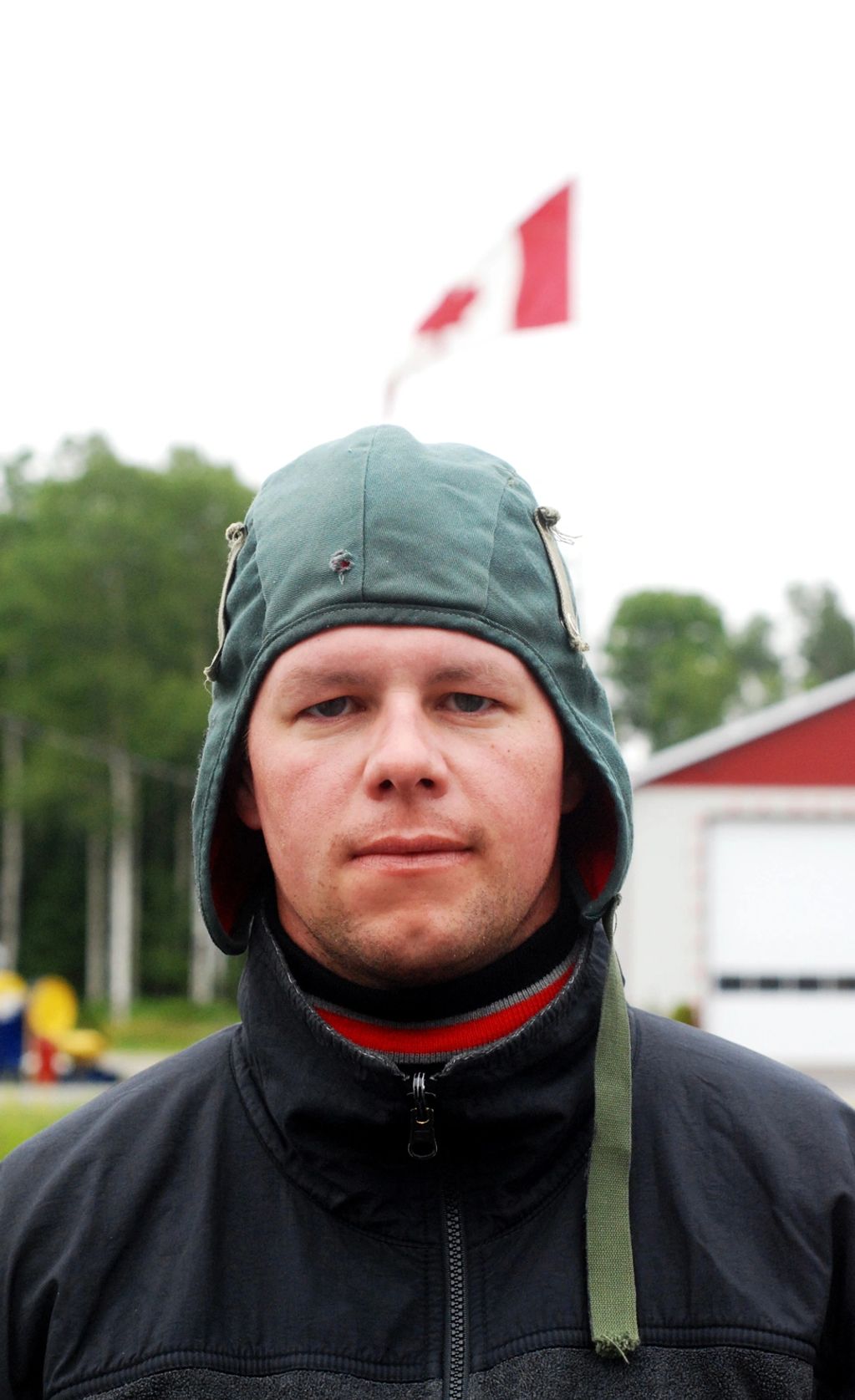 Man in hat with stern look with Canadian flag flying in the background