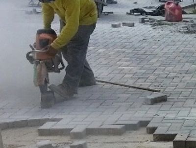 Workers cutting and laying bricks on a driveway.