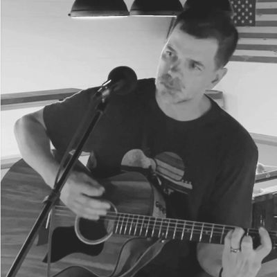 Man playing acoustic guitar and singing into a microphone indoors.