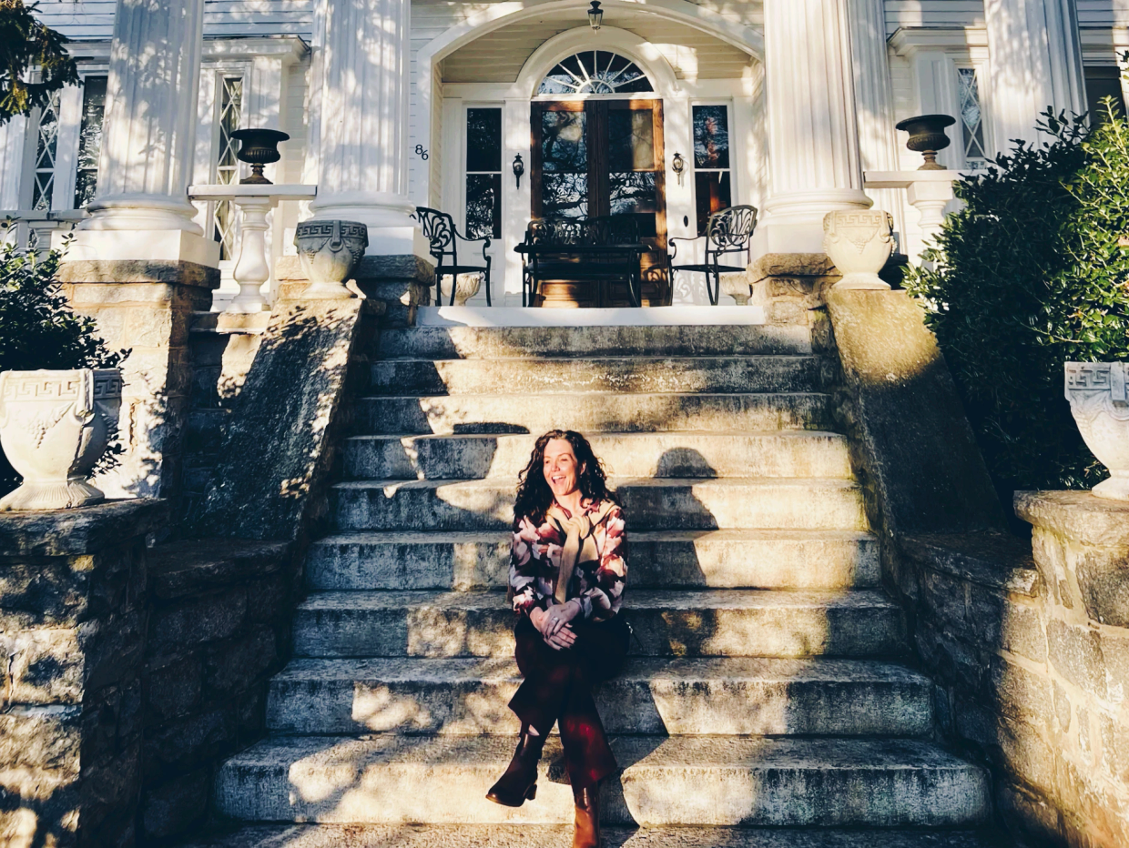Woman sitting on stone steps of a grand white building.