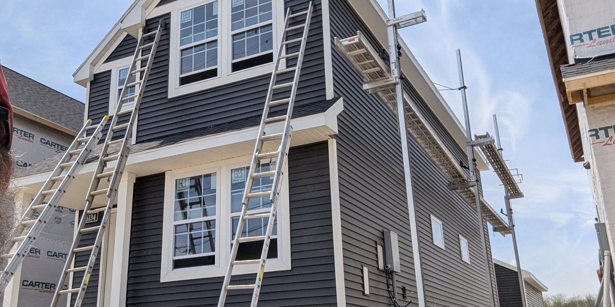 New house siding installation with multiple ladders and scaffolding set up.