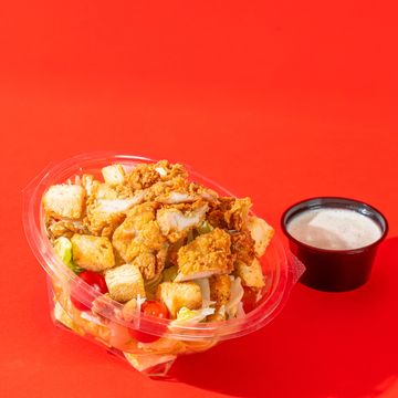 Fried chicken salad with croutons and dressing on vibrant red background.