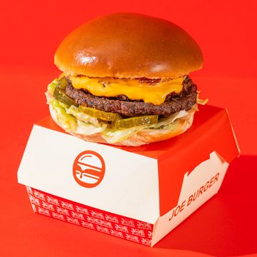 Cheeseburger with pickles and lettuce in a Joe Burger box against red background.