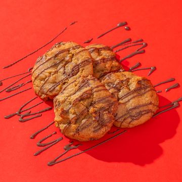 Chocolate chip cookies drizzled with chocolate on a bright red background.