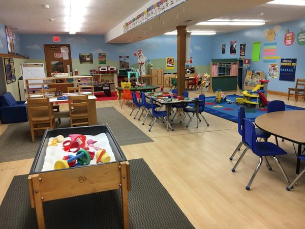 Colorful and organized preschool classroom with play areas and child-sized furniture.