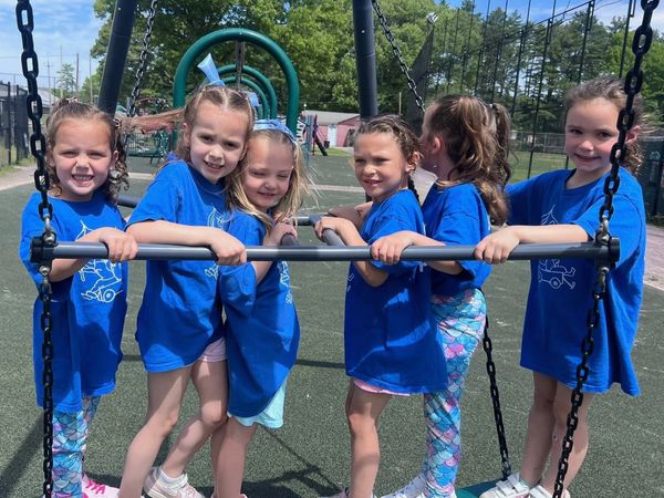 Six young girls in matching blue shirts on a playground swing set.