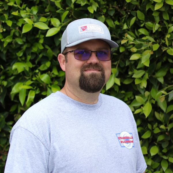 Man wearing glasses and cap smiling outdoors.