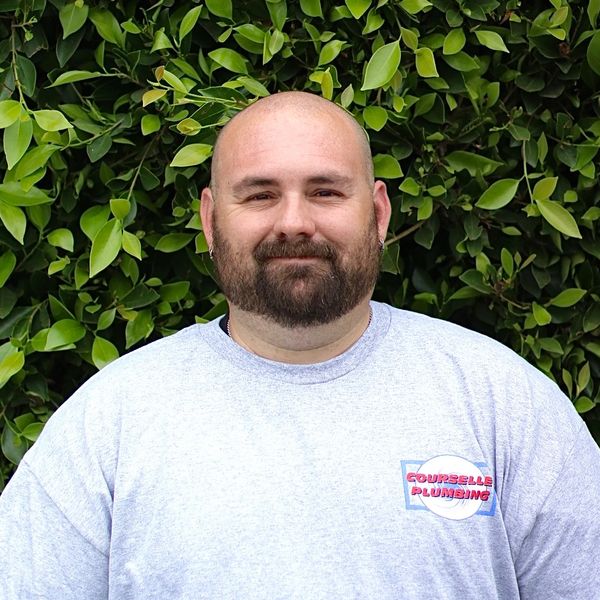 Smiling bald man with beard in front of green foliage.