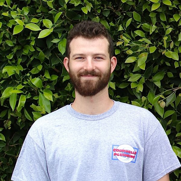Smiling man with beard in front of green foliage.