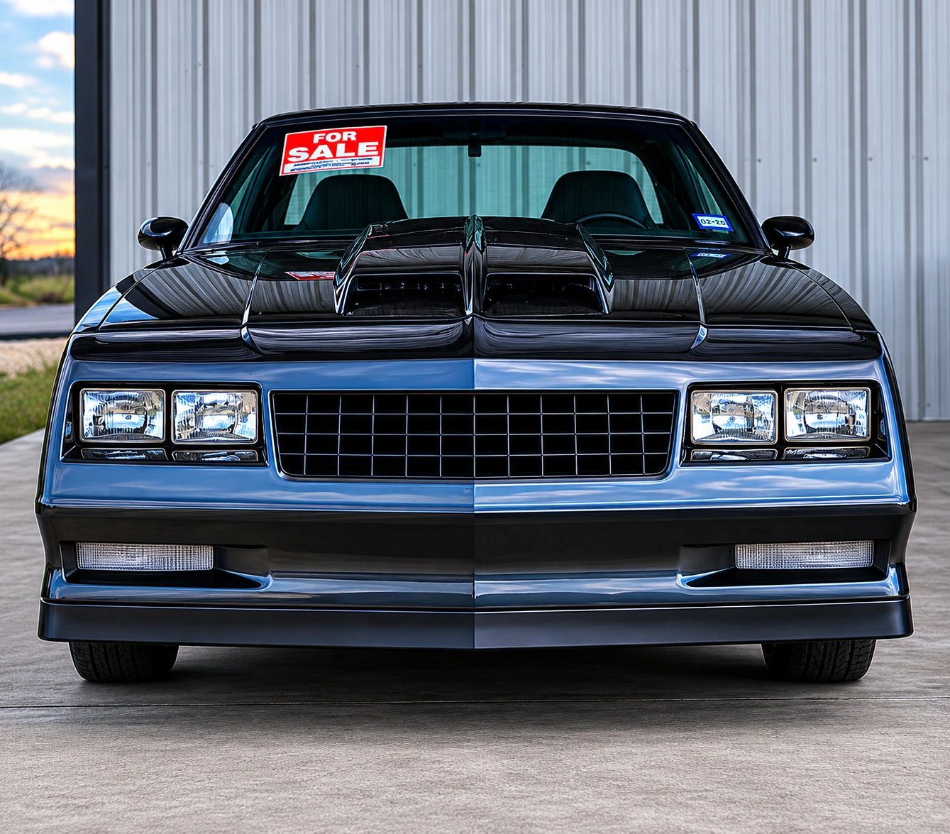 Front view of a sleek black muscle car with a 'For Sale' sign on the windshield.