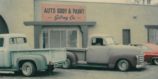 Vintage pickup trucks parked outside an auto body and paint shop.