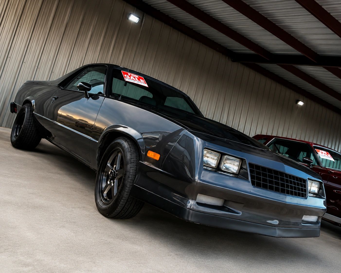 Sleek black vintage car with a 'For Sale' sign in a covered parking area.