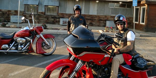 Two men with helmets posing on red motorcycles in a parking lot.