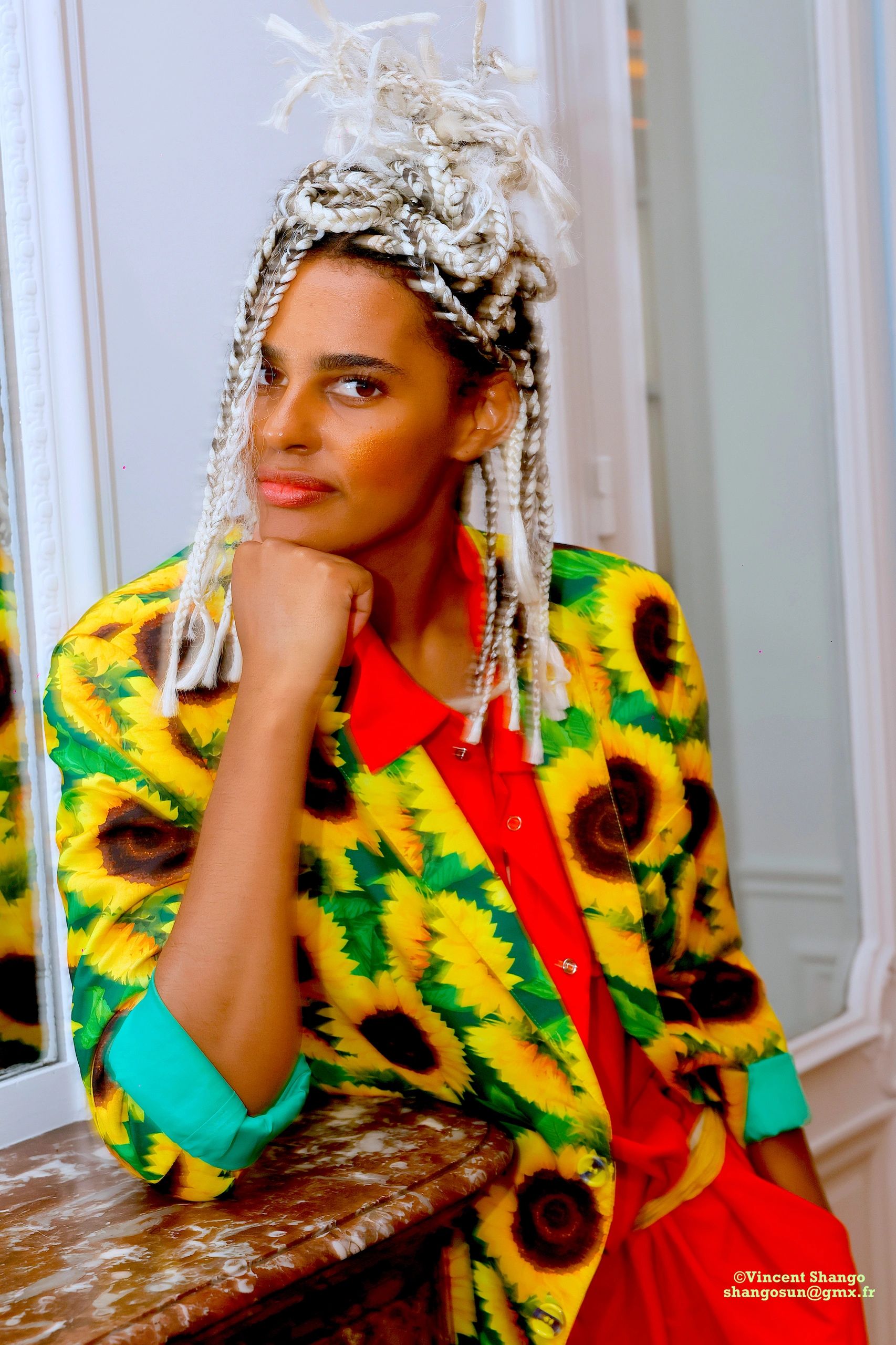 Person with braided hair wearing a vibrant sunflower-patterned blazer and red shirt.