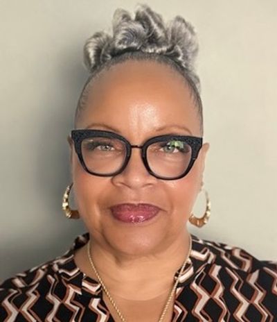 Smiling woman with glasses and hoop earrings in patterned outfit.