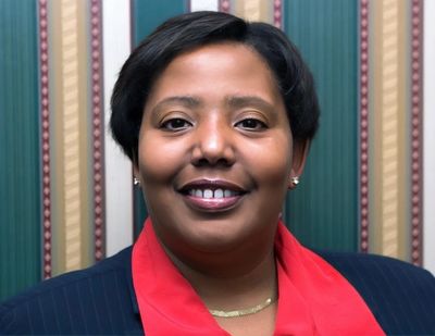 Smiling woman in a red scarf and dark blazer against patterned background.