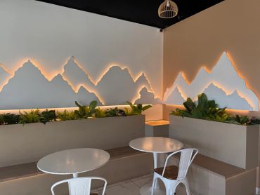 Modern cafe interior with mountain-shaped wall lights and white metal chairs.