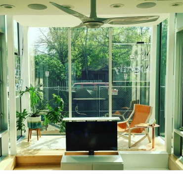Bright living room with large glass windows, plants, and a TV.