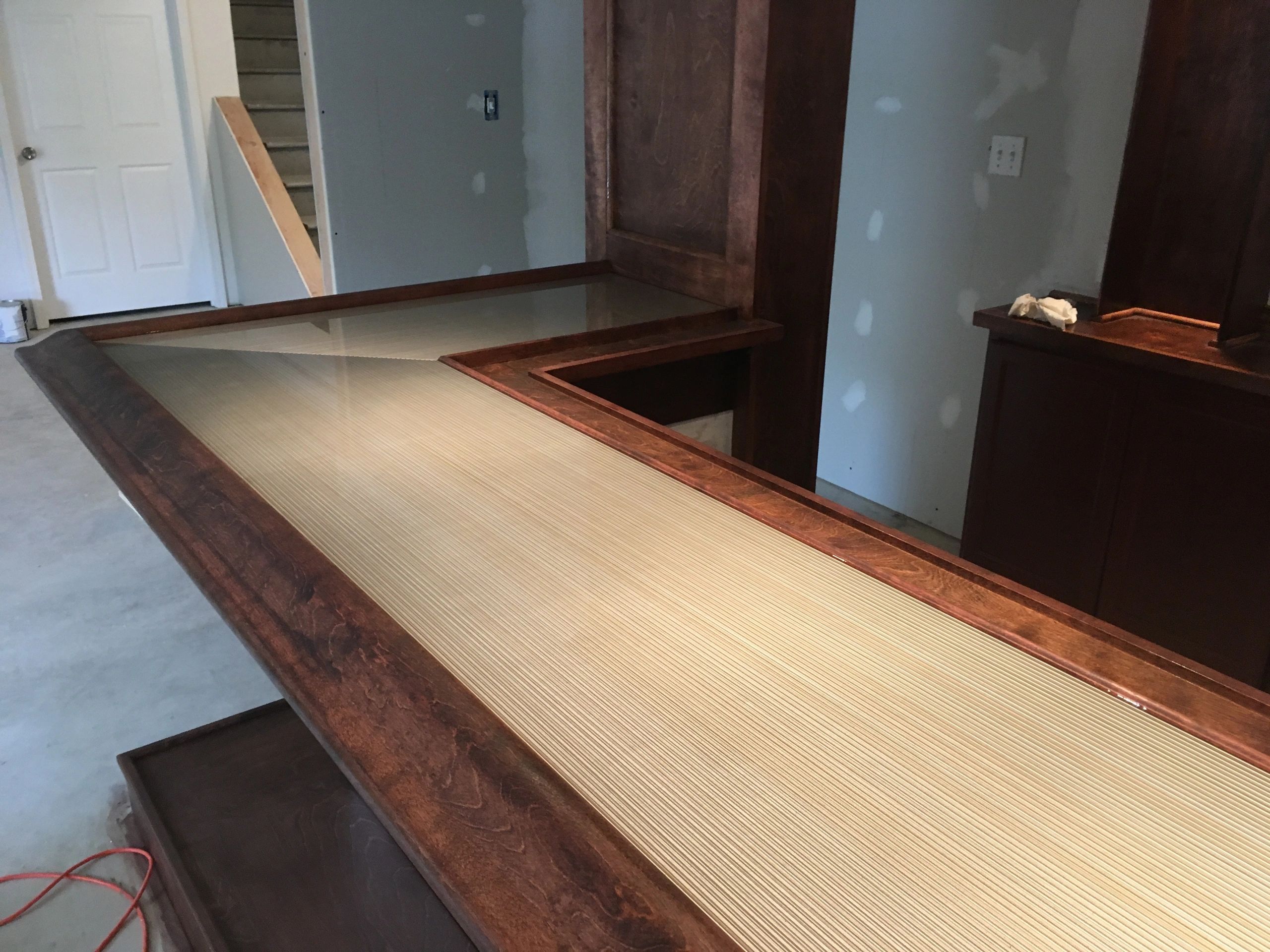 Wooden bar counter with a glass top in an unfinished room.