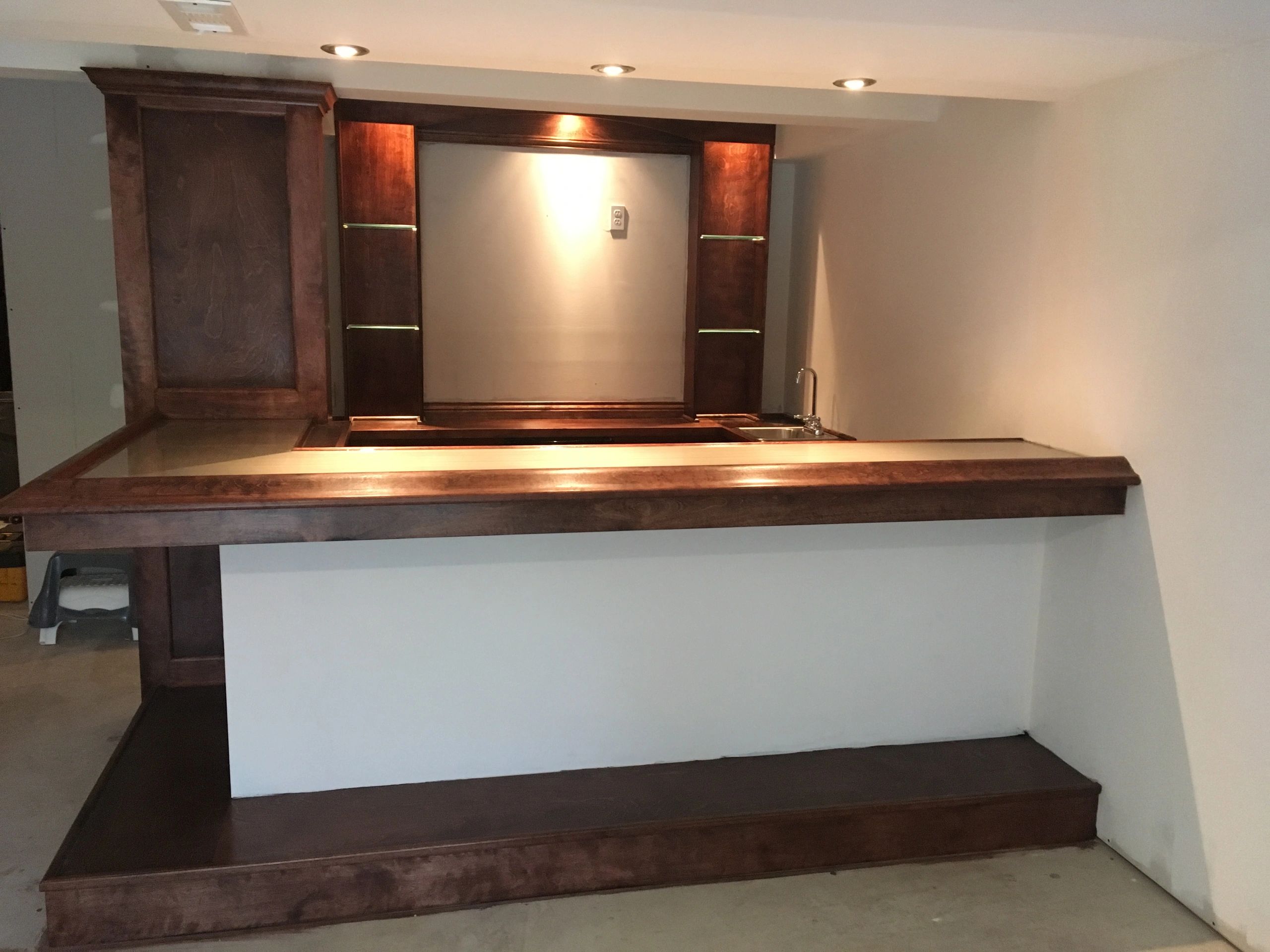 Unfinished wooden home bar with shelves and a small sink in a basement.
