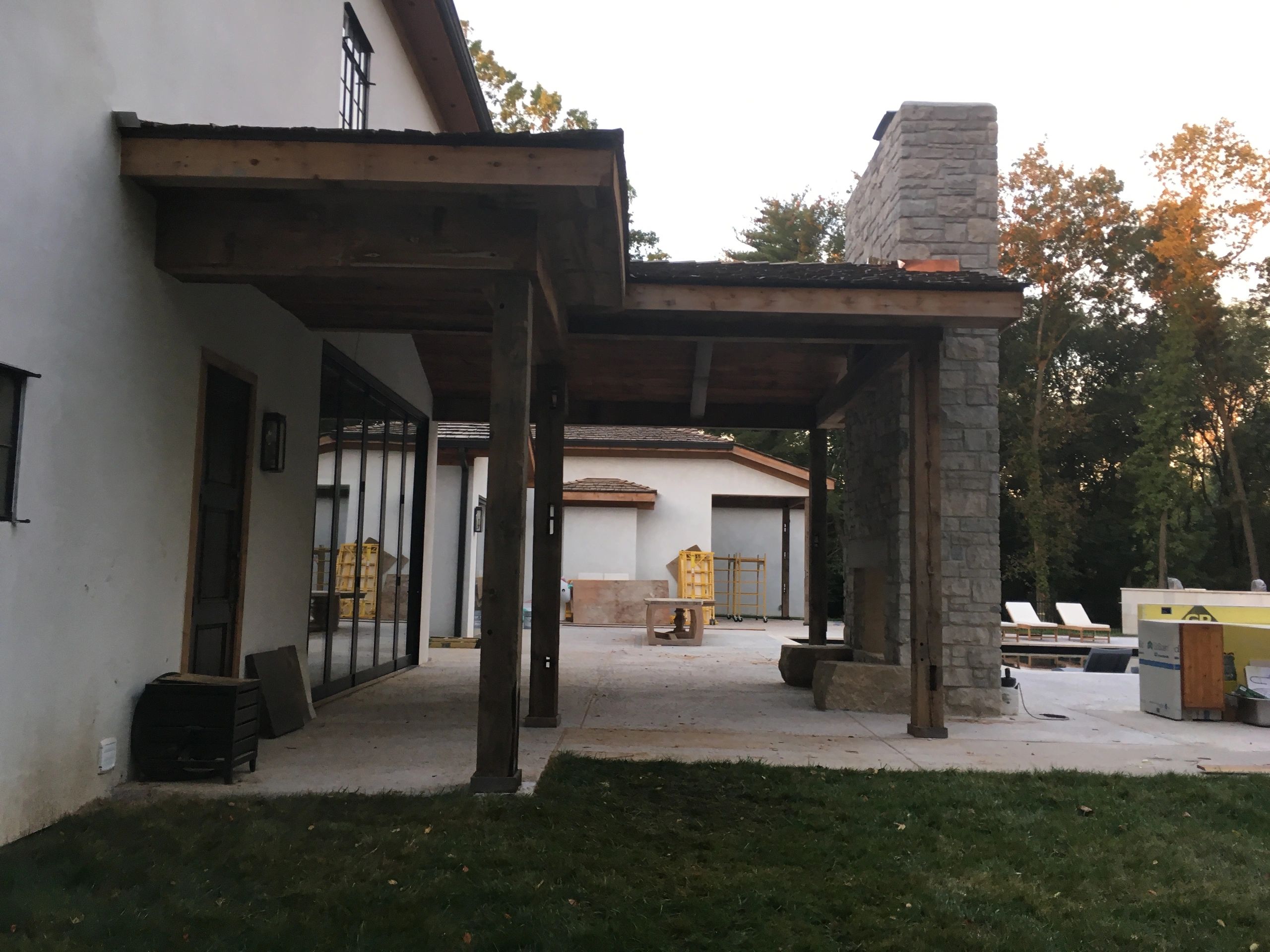 Rustic outdoor patio with wooden beams and stone fireplace under construction.