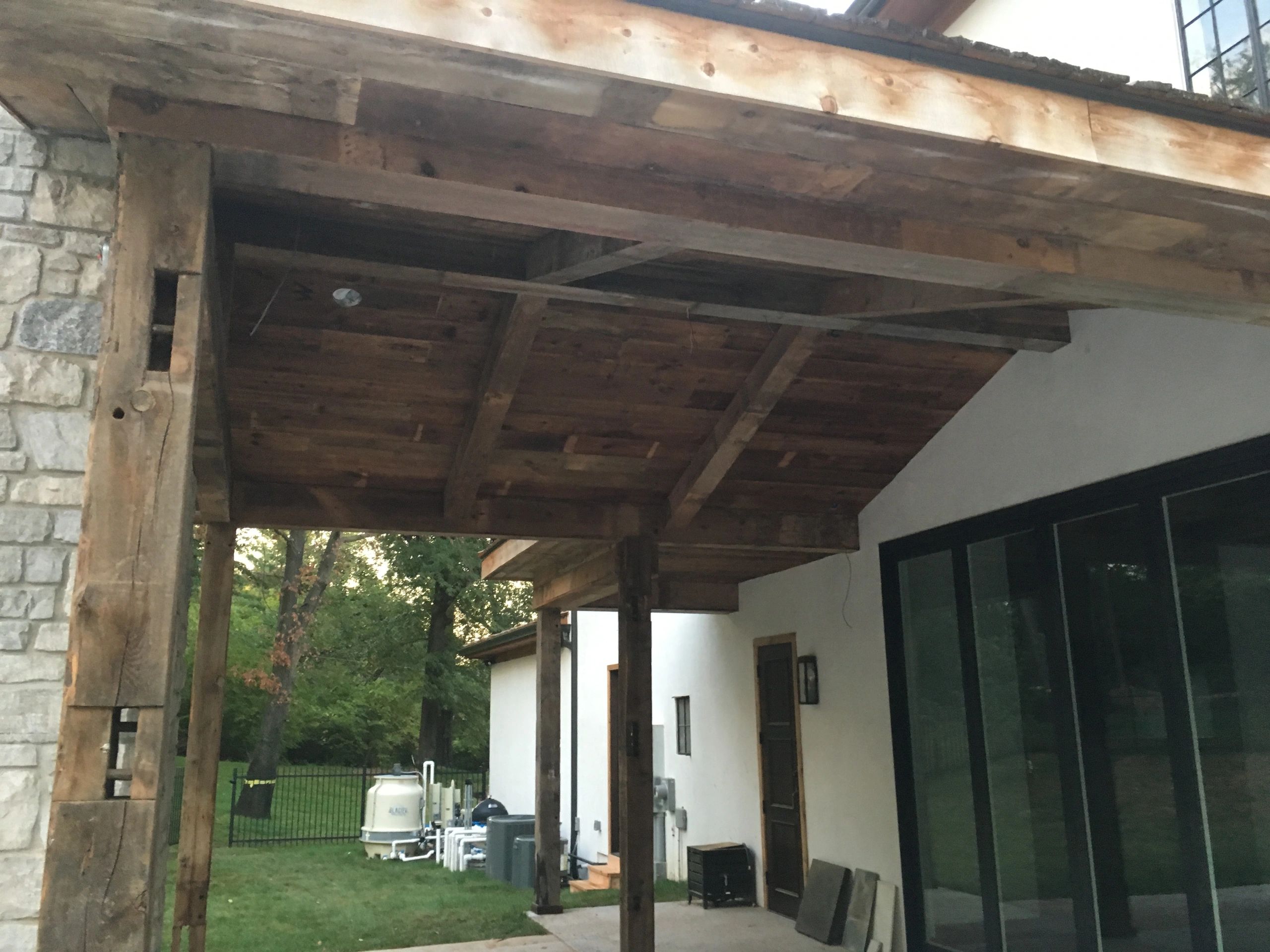 Rustic wooden porch roof with stone and white walls of a house.