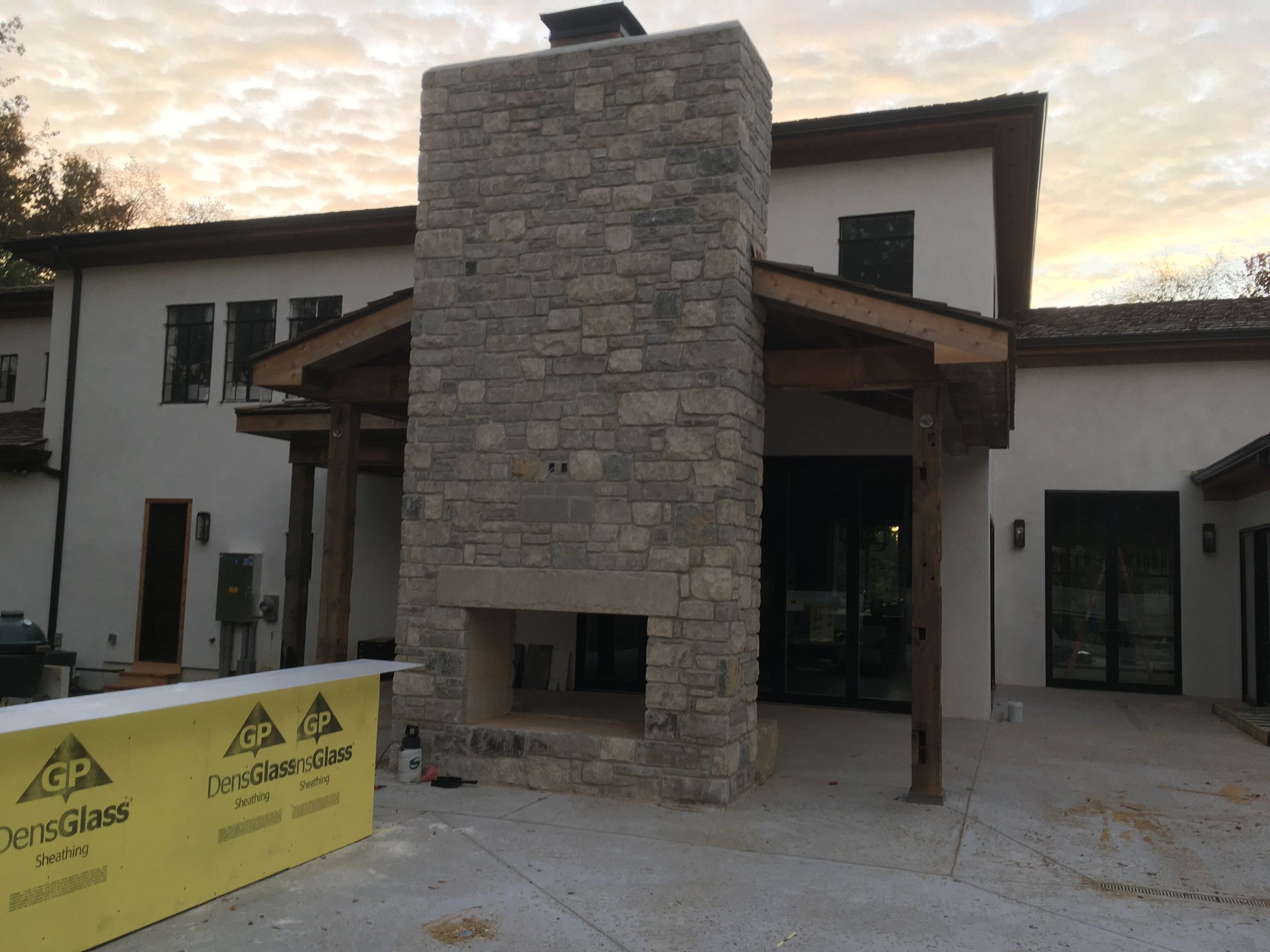 Stone outdoor fireplace in front of a modern house at sunset.