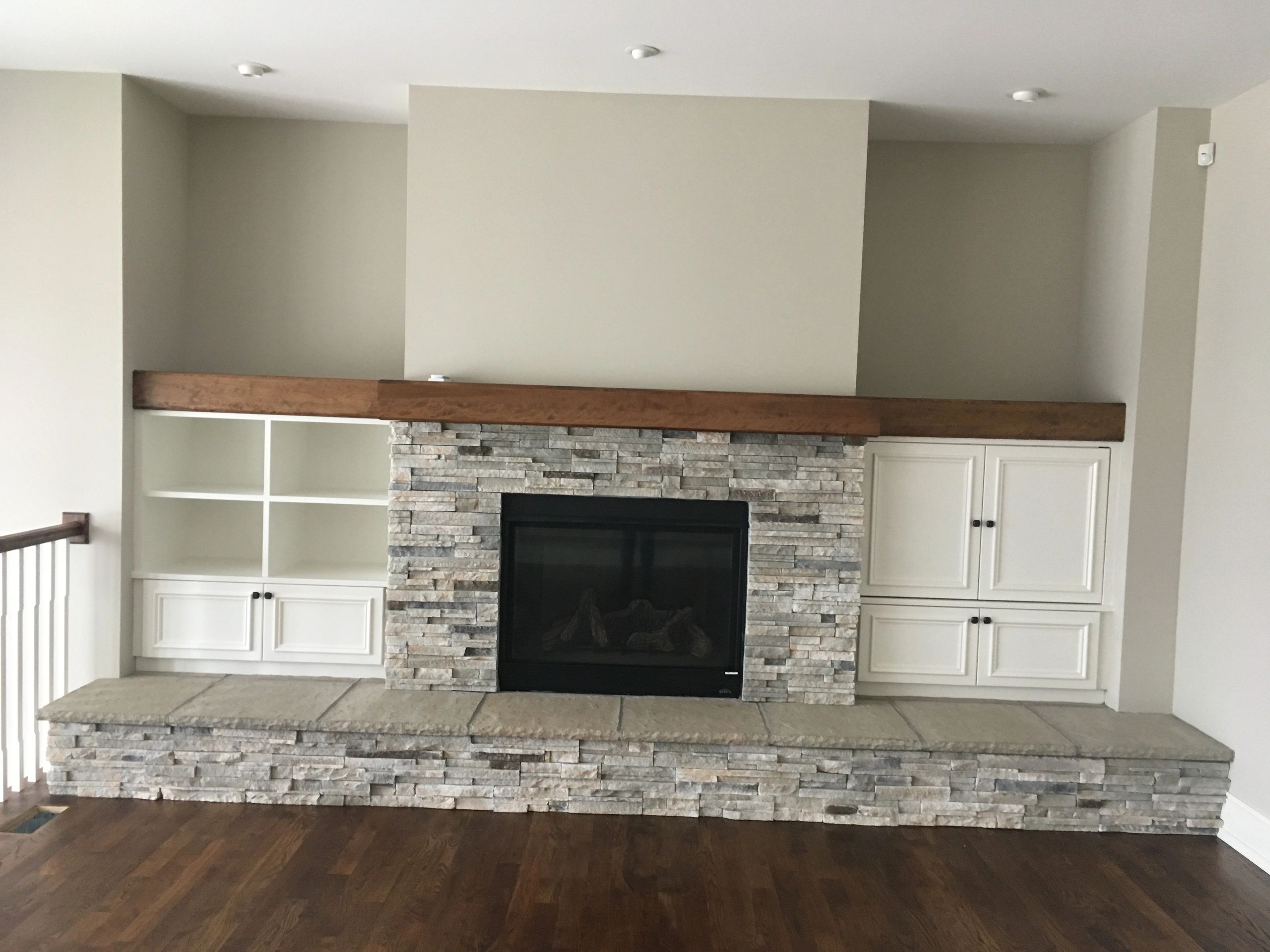 Modern stone fireplace with wooden mantle and white cabinetry.