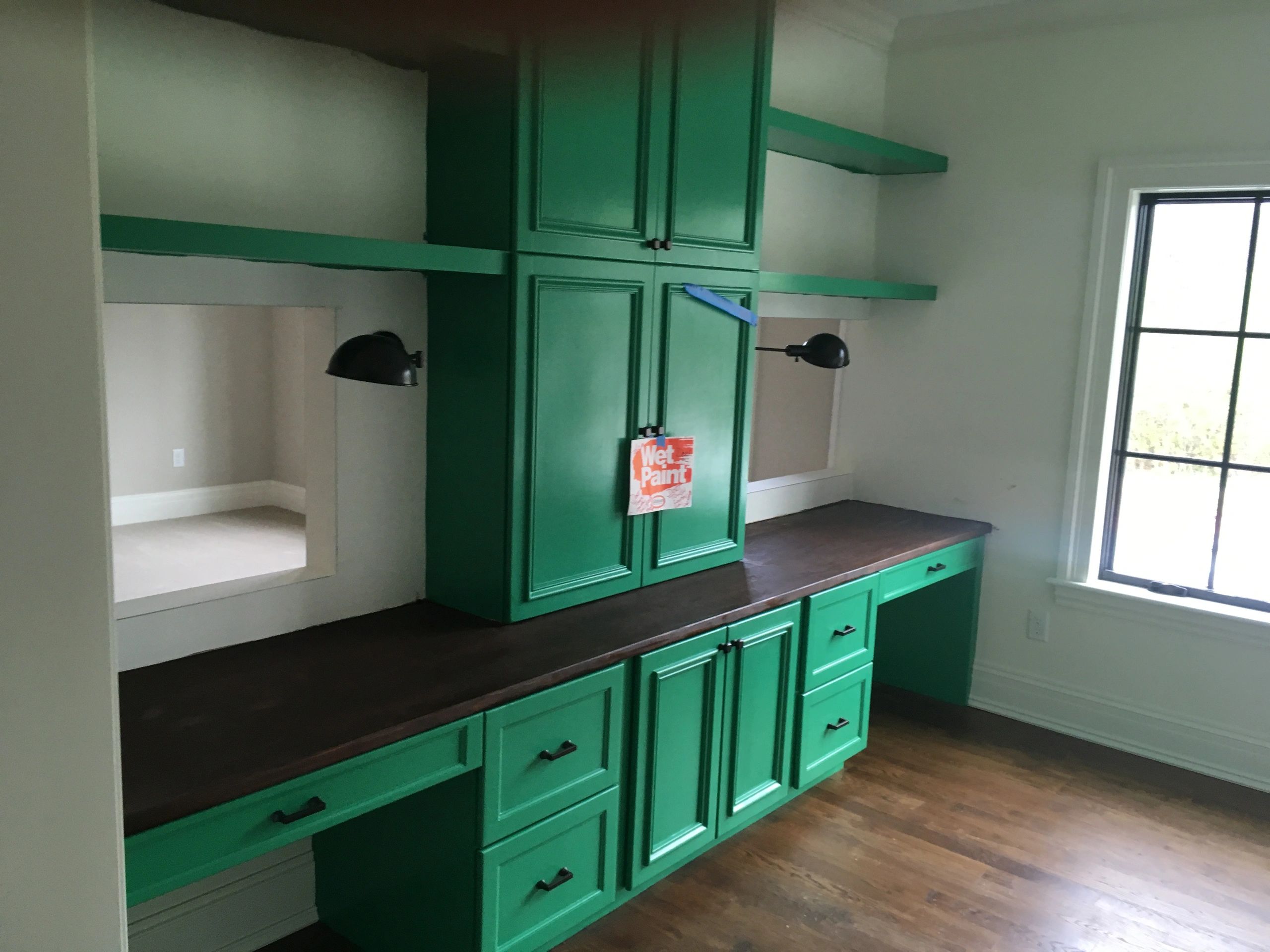 Freshly painted green cabinets with a wet paint sign in a bright room.