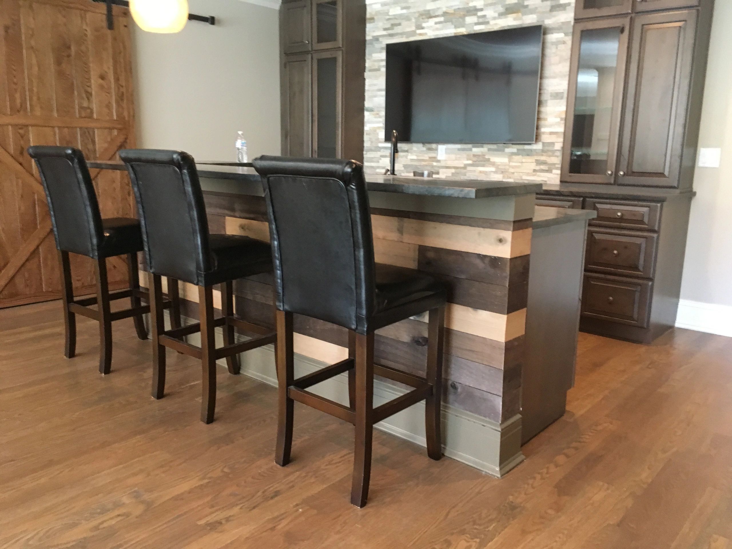 Wood-paneled kitchen bar with black leather stools and a mounted TV.