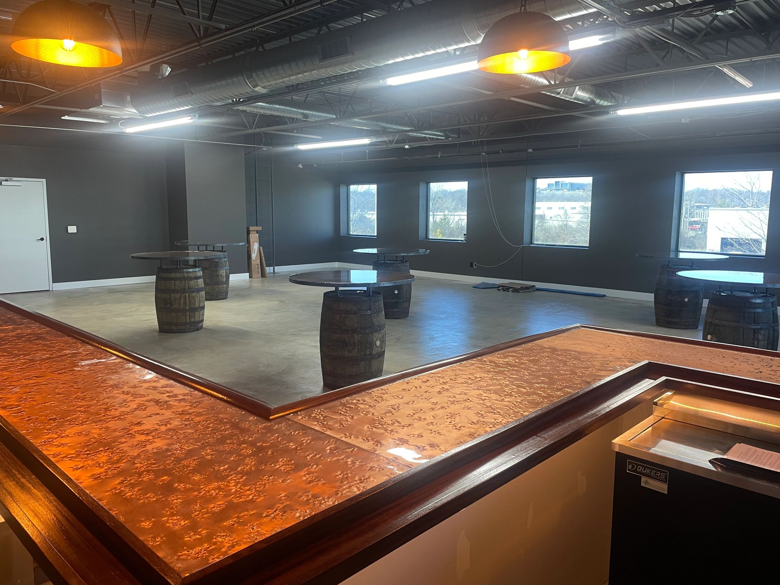 Modern bar area with copper countertops and barrel-style tables in a spacious room.
