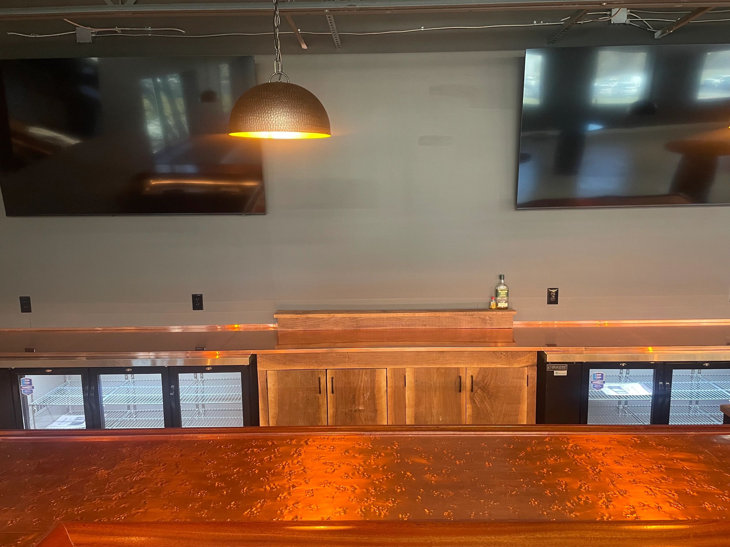 Empty bar with wooden cabinets, two TVs, and a single bottle on the counter.