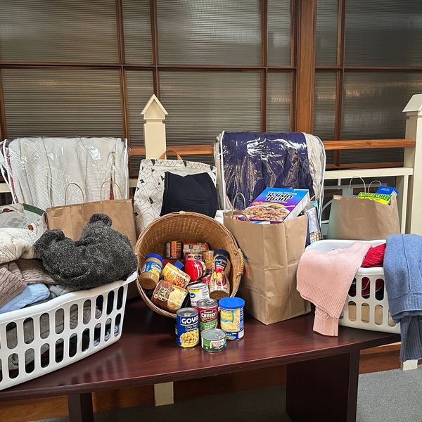 Donation setup with clothes, canned food, and grocery bags on a table.