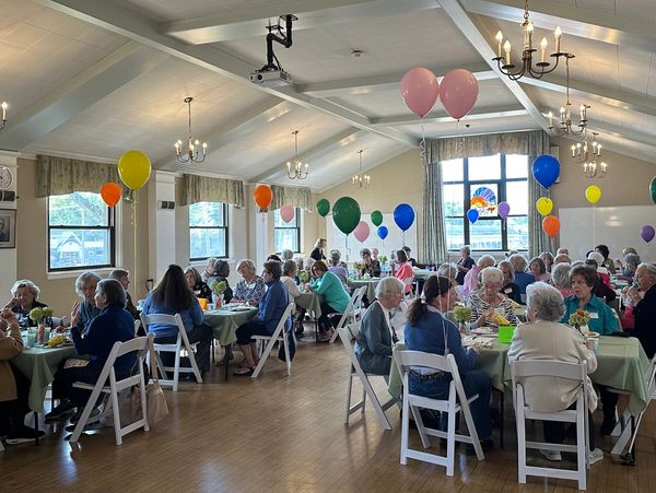 Seniors gathered in a decorated hall for a social event with colorful balloons.