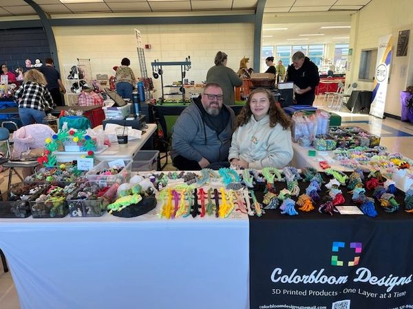 Two people at a Colorbloom Designs booth with 3D printed colorful items.