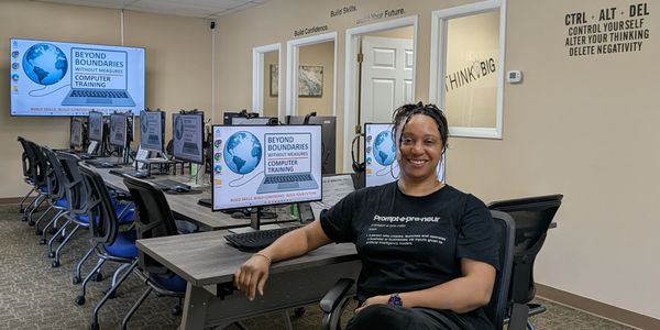 Woman smiles confidently in a computer training classroom with motivational wall quotes.