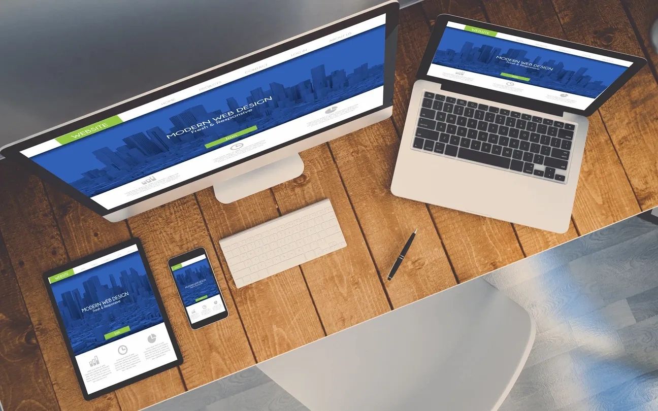Multiple devices displaying a modern web design on a wooden desk.