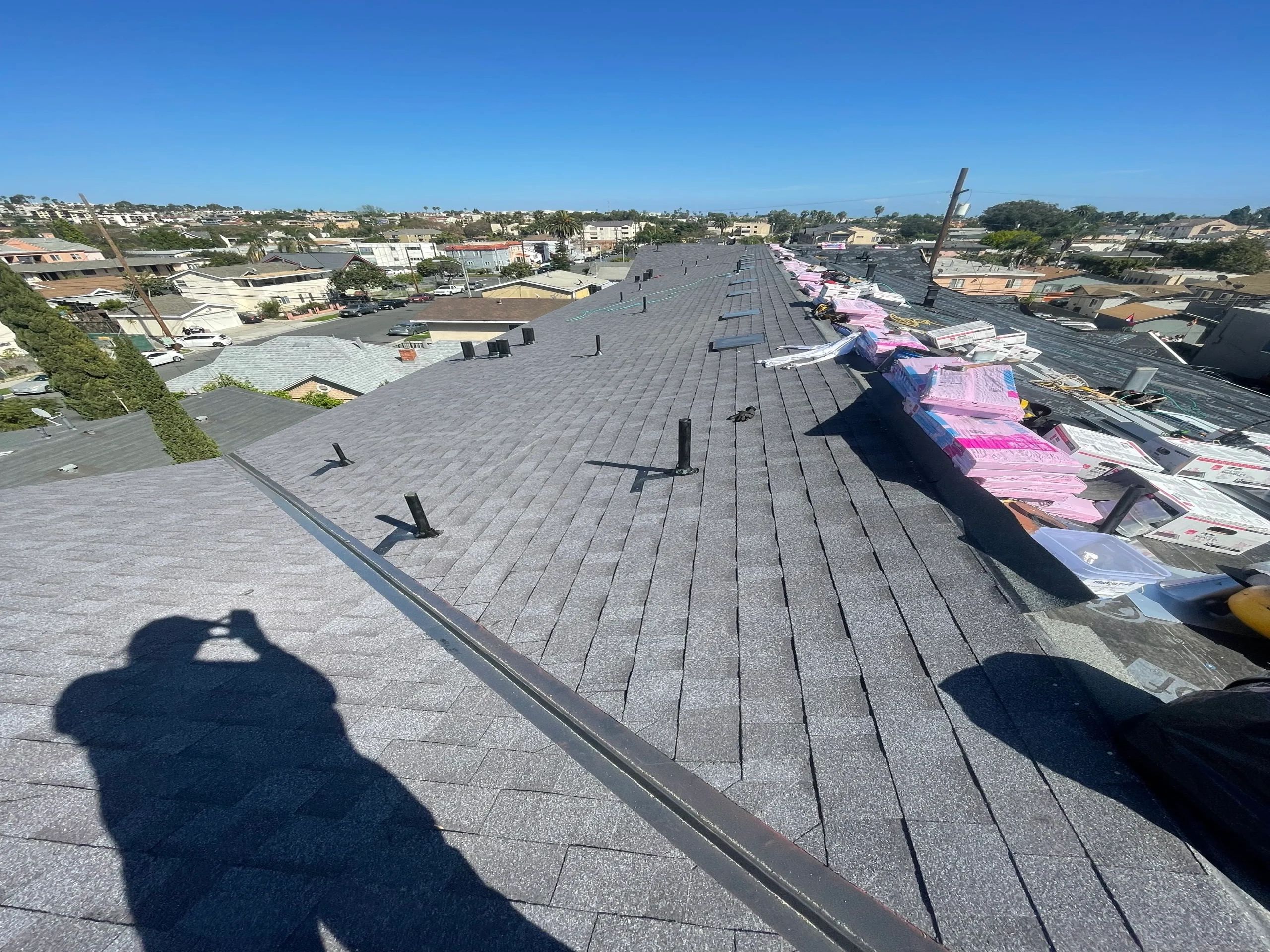 Newly shingled roof under clear blue sky with roofing materials stacked.