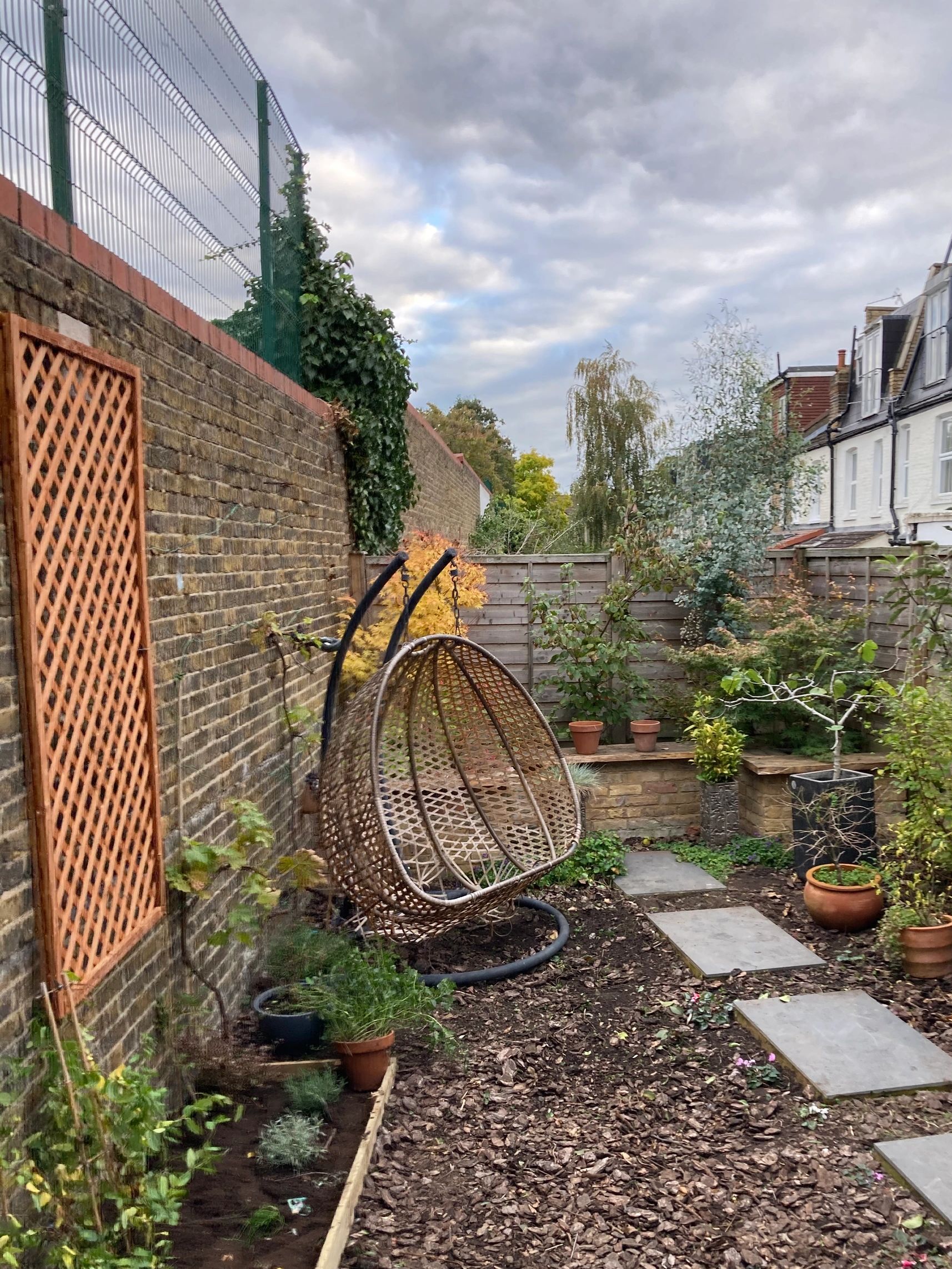 Wooden rocking chair in a small urban garden setting with freshly laid bark and raised bed.