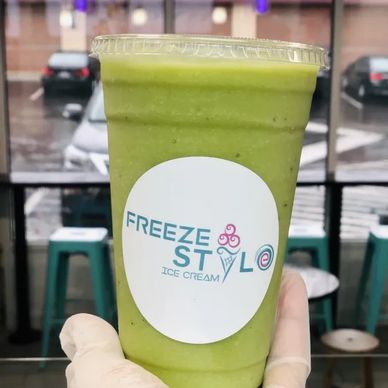 Green smoothie in branded cup held by gloved hand.