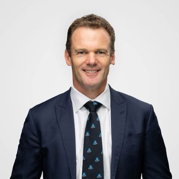 Man in a dark suit and patterned tie smiling at the camera.