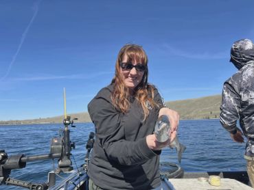 Woman holding a fish on a boat under clear blue sky.